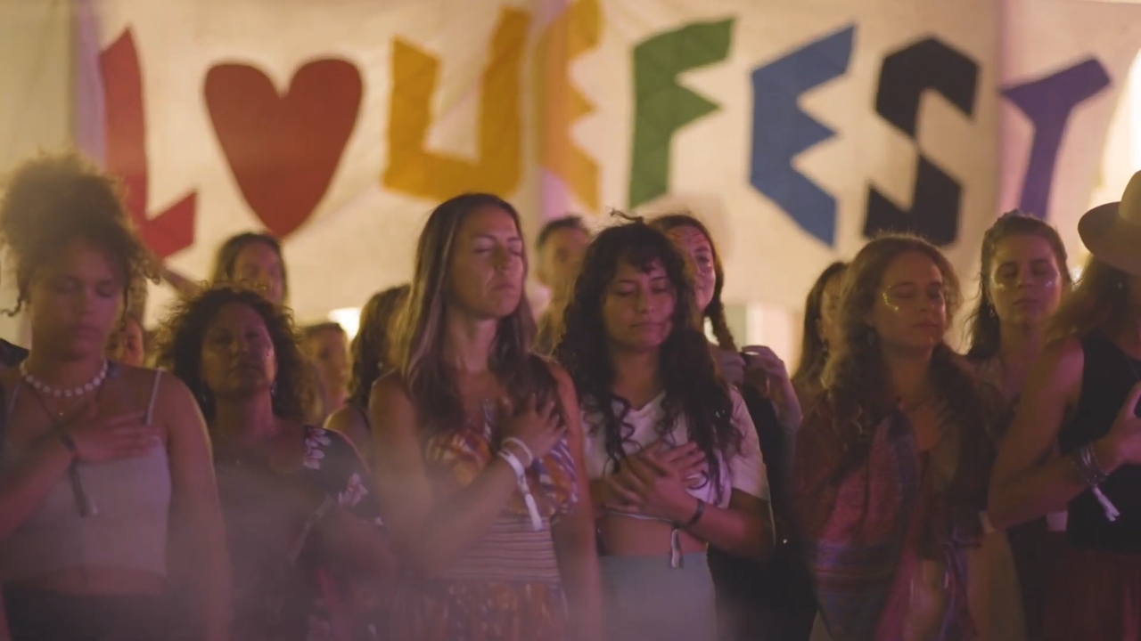 Grupa ljudi na Lovefestu stoji blizu bine i uživa u muzici uz opuštenu atmosferu i svetla u pozadini