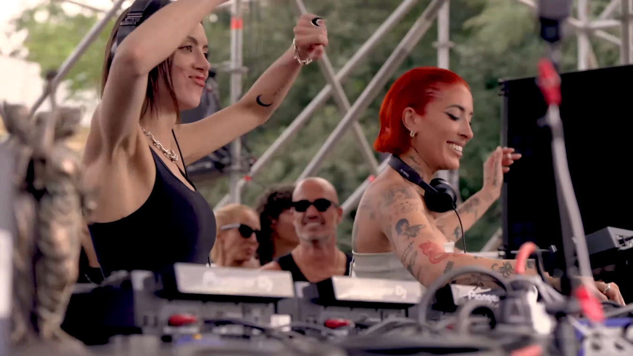 Dve DJ-ke puštaju muziku na otvorenoj bini dok publika uživa u festivalskoj atmosferi